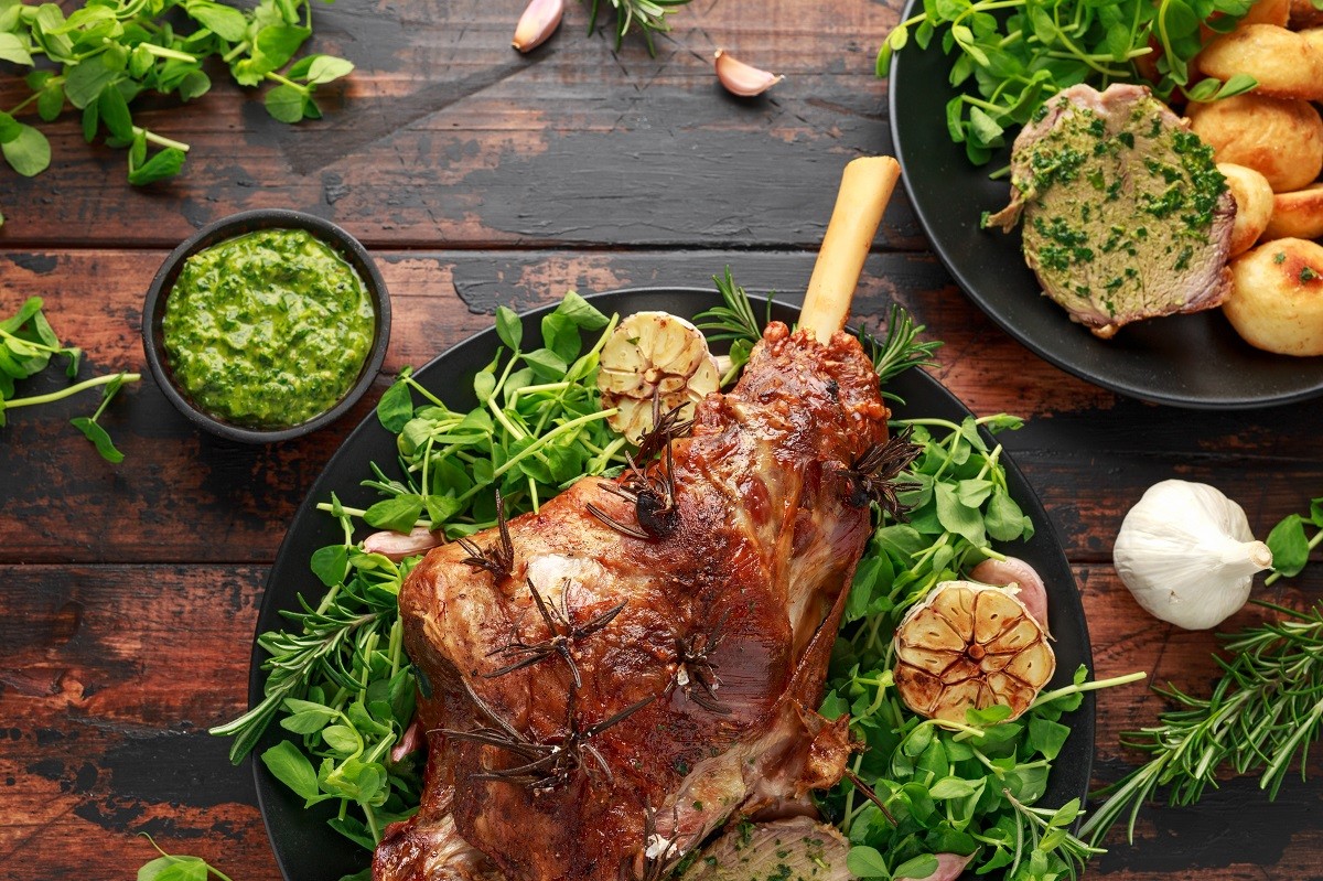 Roast Lamb leg with mint sauce, rosemary and garlic. on black plate, wooden table