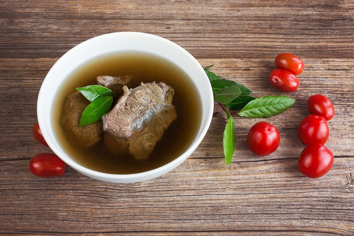 Beef broth with meat and tomatoes on wooden background