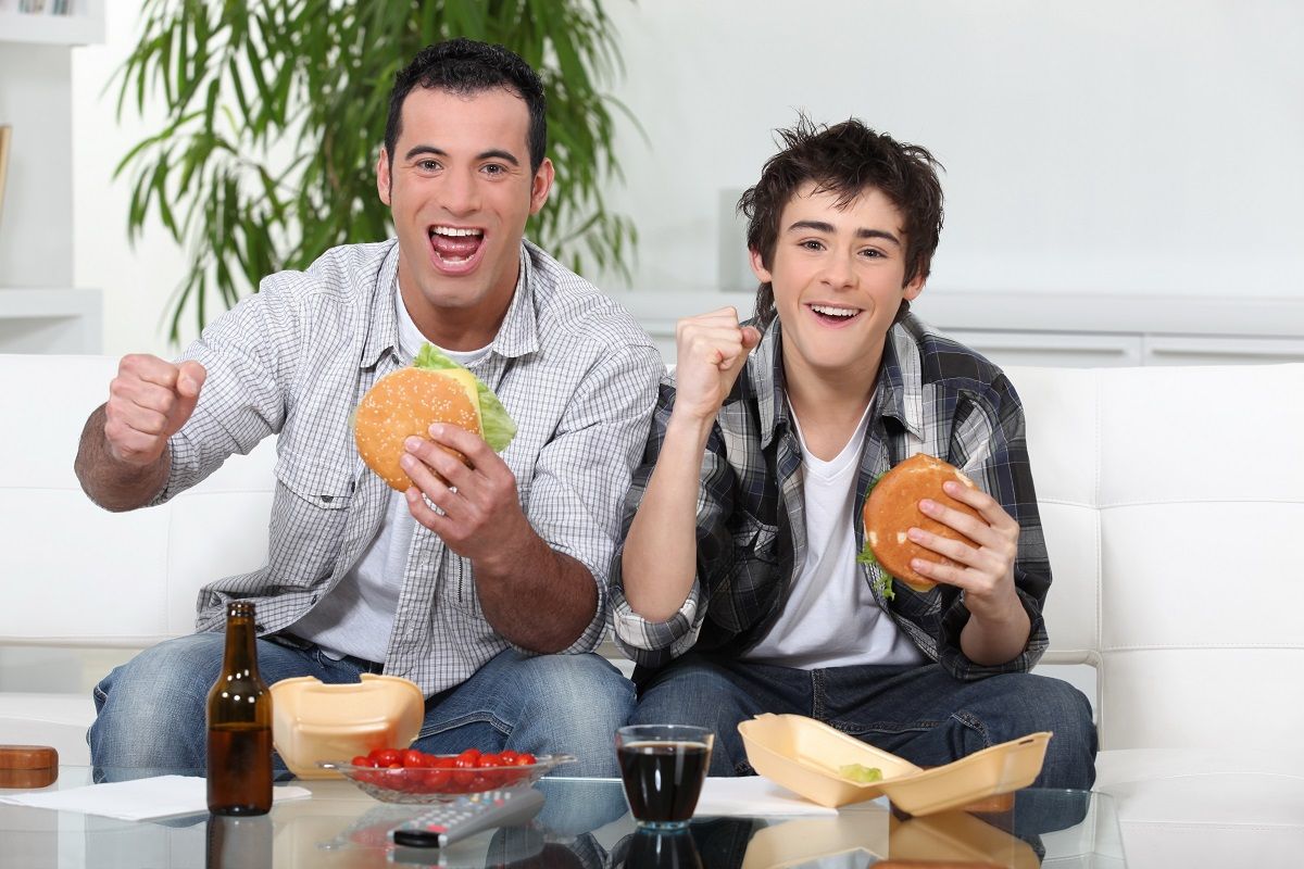 14214627 – father and son eating burgers in front of tv