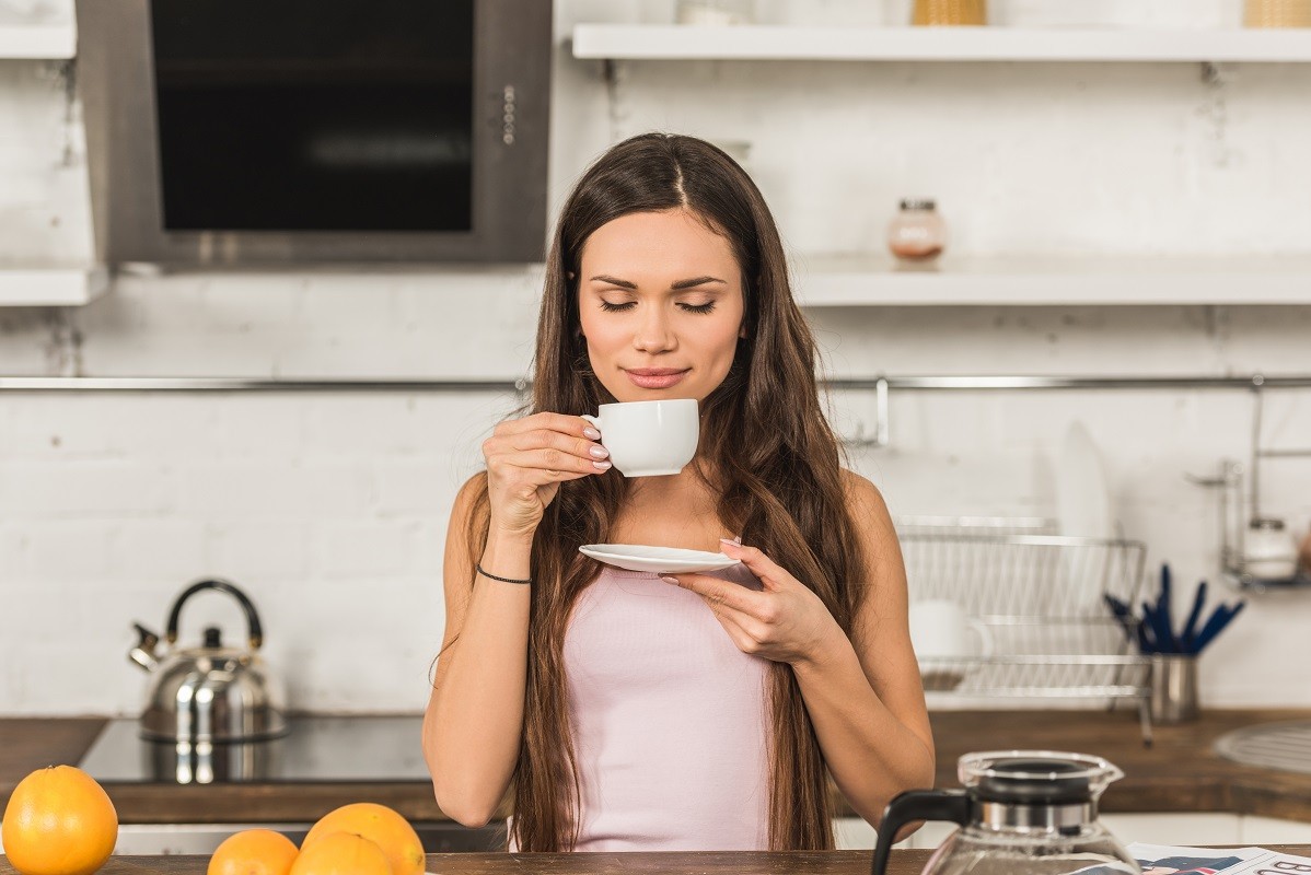 beautiful woman with closed eyes sniffing aromatic coffee in morning at kitchen