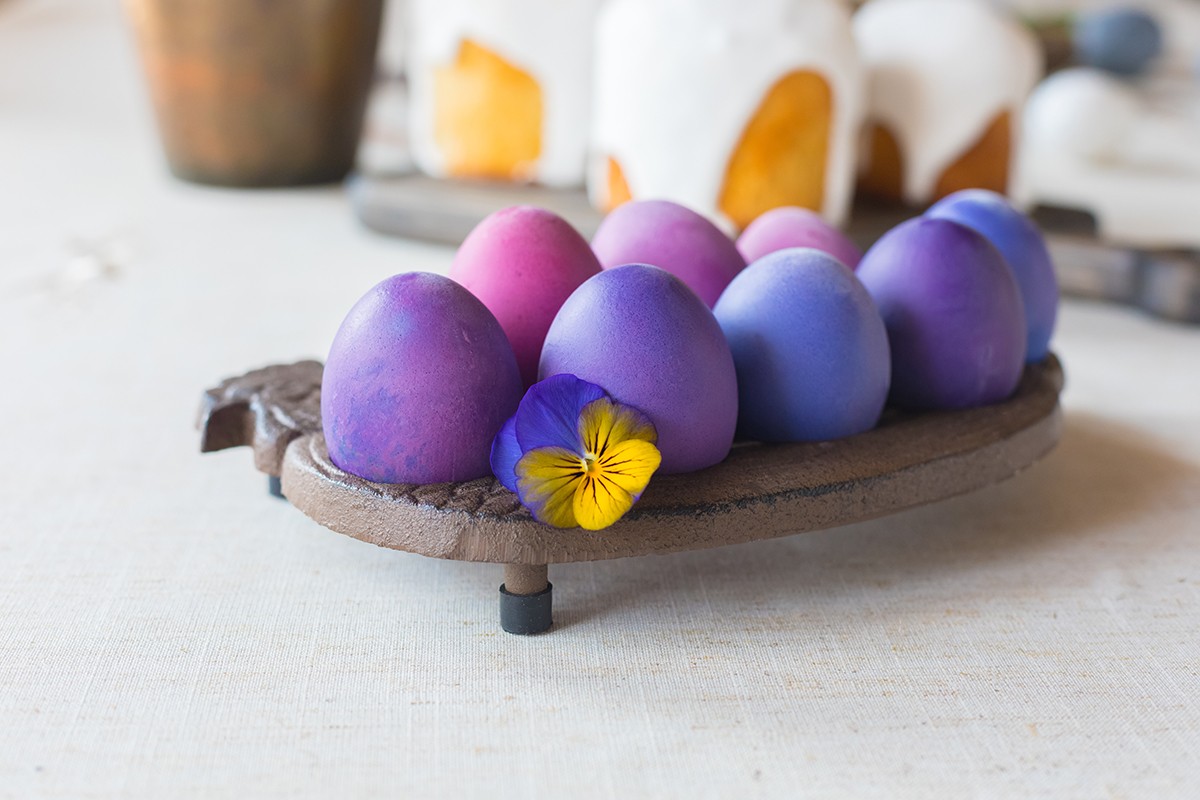Naturally dyed Easter hen’s eggs with a vioet flower on linen background