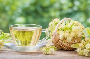 Cup of healthy linden tea and wicker basket with lime flowers, h