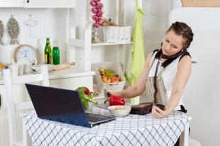 Woman with notebook and phone cooks in kitchen. Isolation period