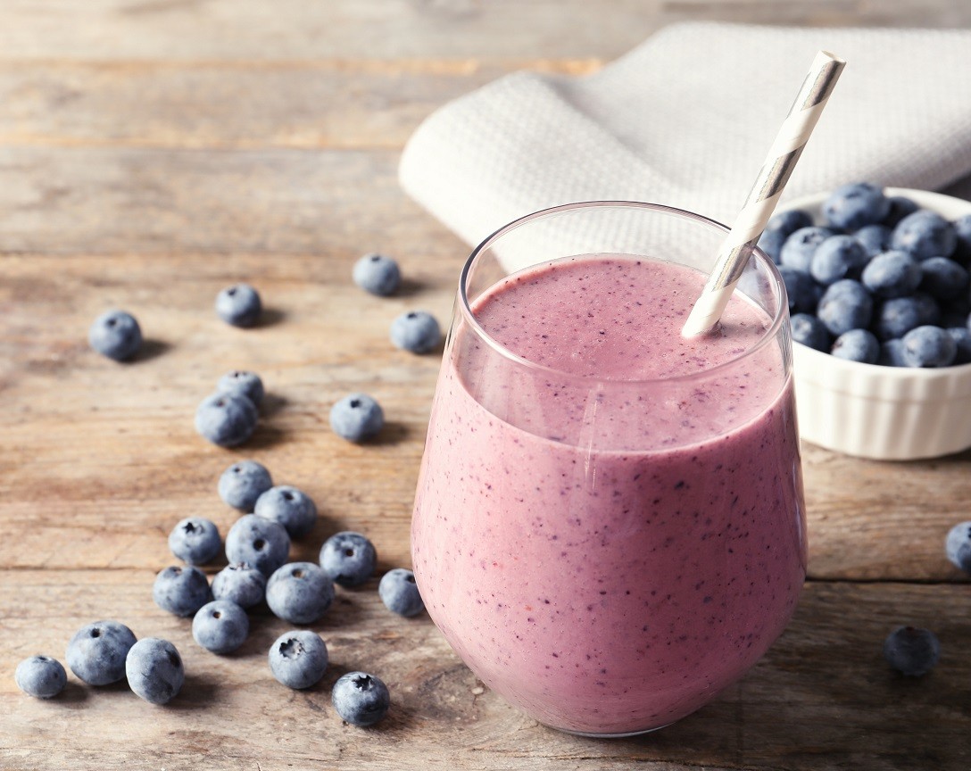 Tasty blueberry smoothie in glass, berries and space for text on wooden table