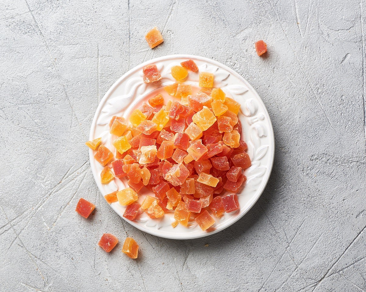 Cubes of dried apricot, mango and papaya on white plate. Candied fruits over gray background with copy space. Top view.