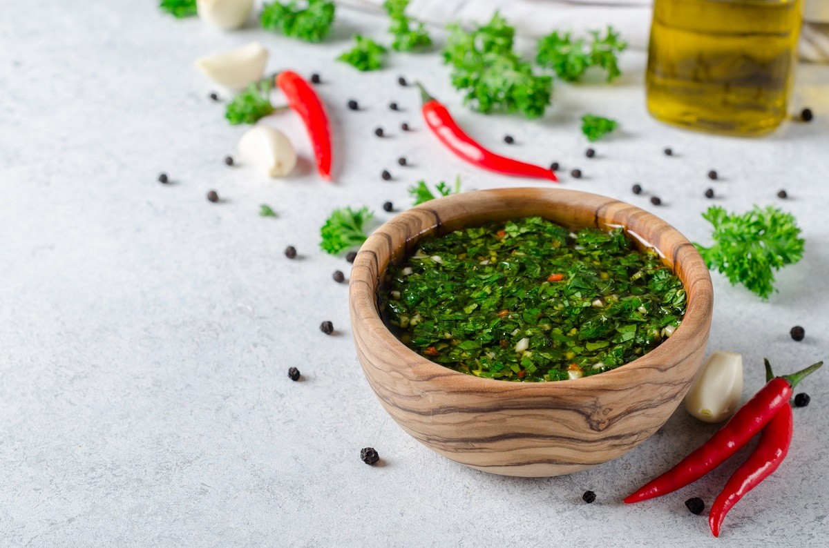 Traditional argentinian chimichurri sauce made of parsley, cilantro, garlic and chili pepper in a wooden bowl. Selective focus, horizontal image