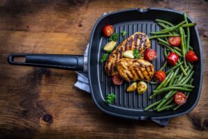 Grilled chicken breast in different variations with cherry tomatoes, green French beans, garlic herbs cut lemon on a wooden board or teflon pan