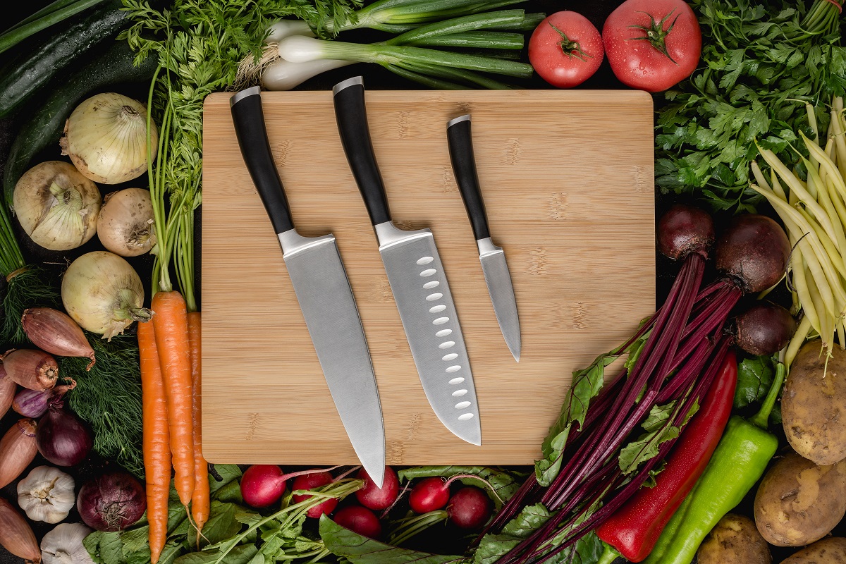Kitchen Knives Set on Wood Cutting Board with Fresh Vegetables. Vegan Raw Food. Healthy Eating Concept.
