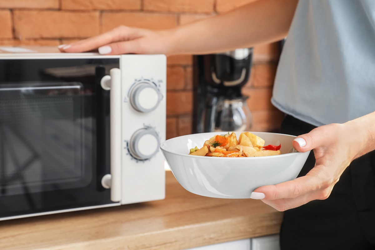 Woman,Holding,Bowl,With,Delicious,Food,Near,Counter,With,Microwave