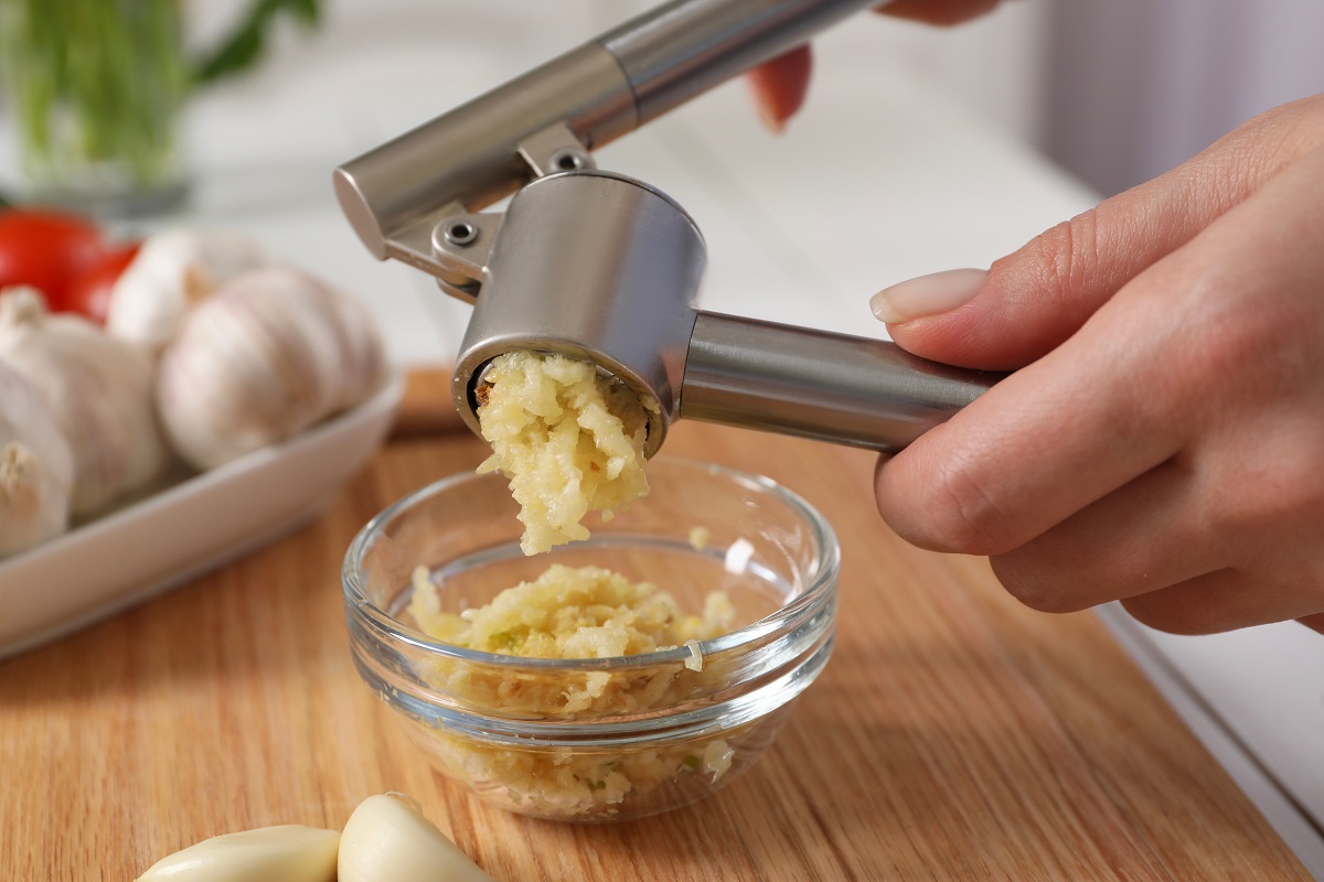 Woman,Squeezing,Garlic,With,Press,At,Wooden,Table,,Closeup