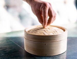 Hand,Holding,Bamboo,Steamer,At,Table