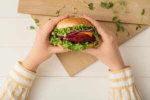 Woman,Holding,Tasty,Vegetarian,Burger,On,White,Wooden,Background