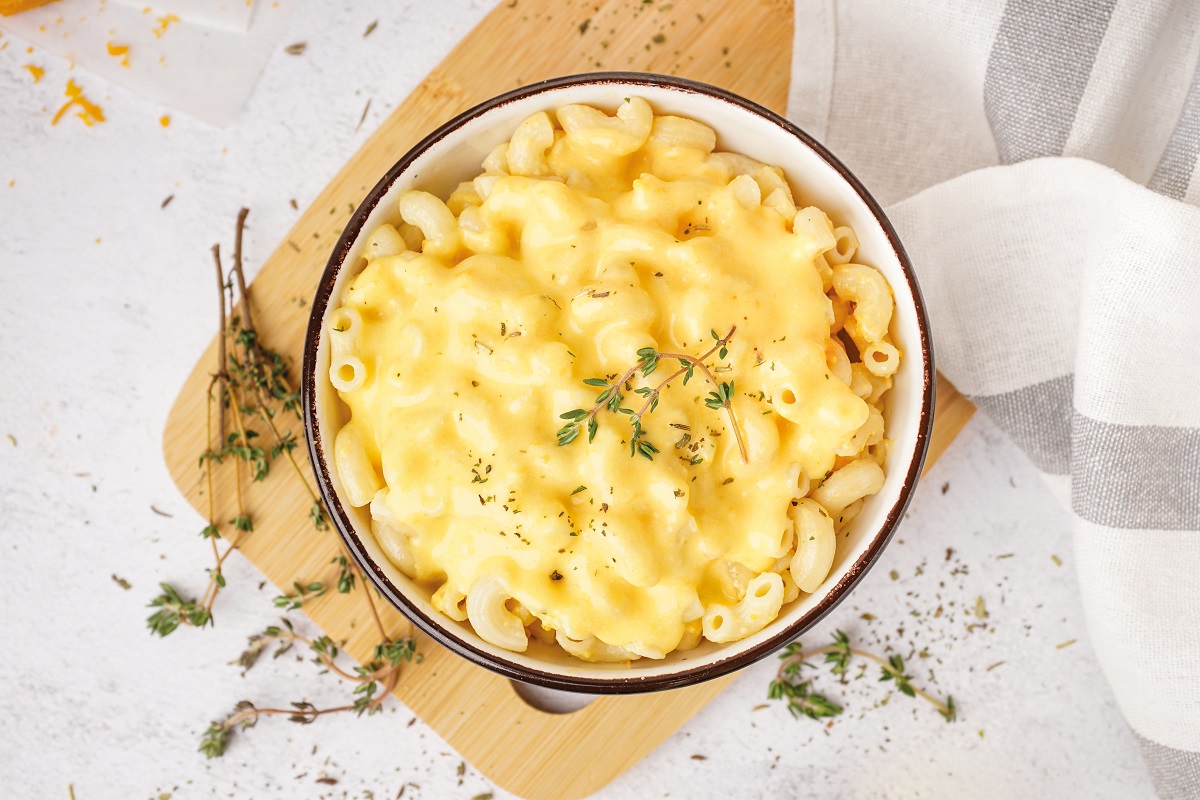 Bowl of tasty Italian pasta with Cheddar cheese on light backgro