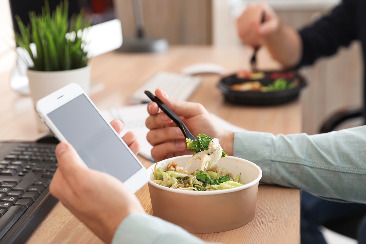 Office,Employee,With,Smartphone,Having,Lunch,At,Workplace,,Closeup.,Food