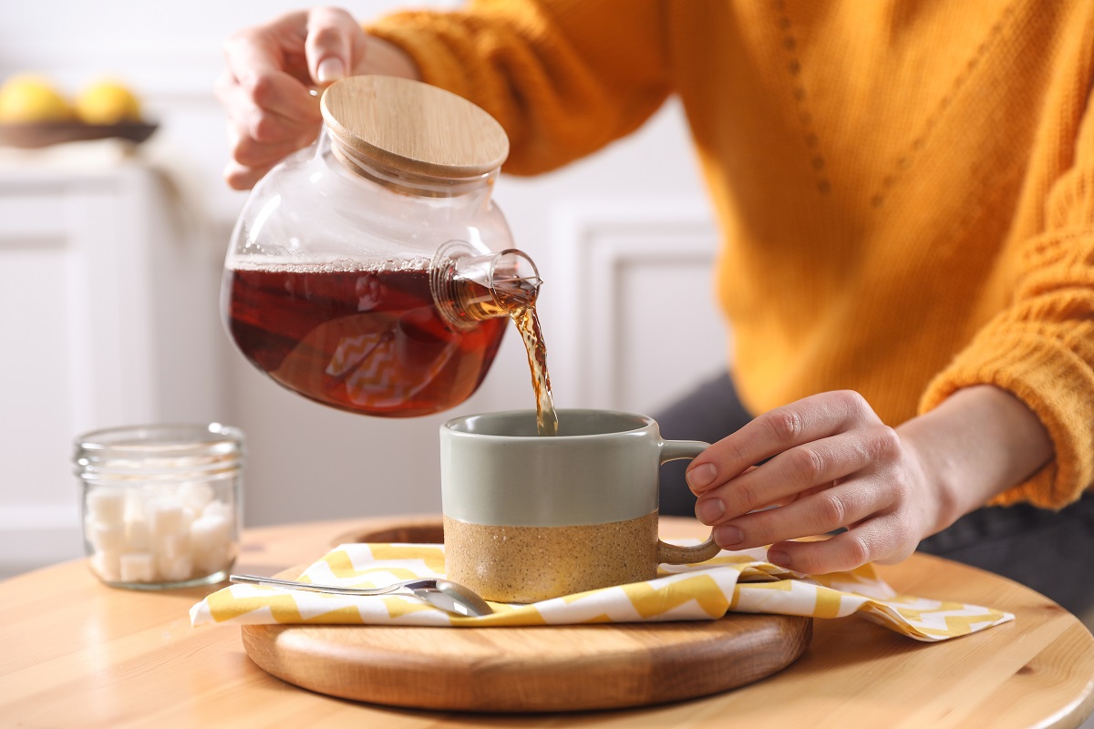 Woman,Pouring,Hot,Tea,Into,Cup,At,Wooden,Table,,Closeup