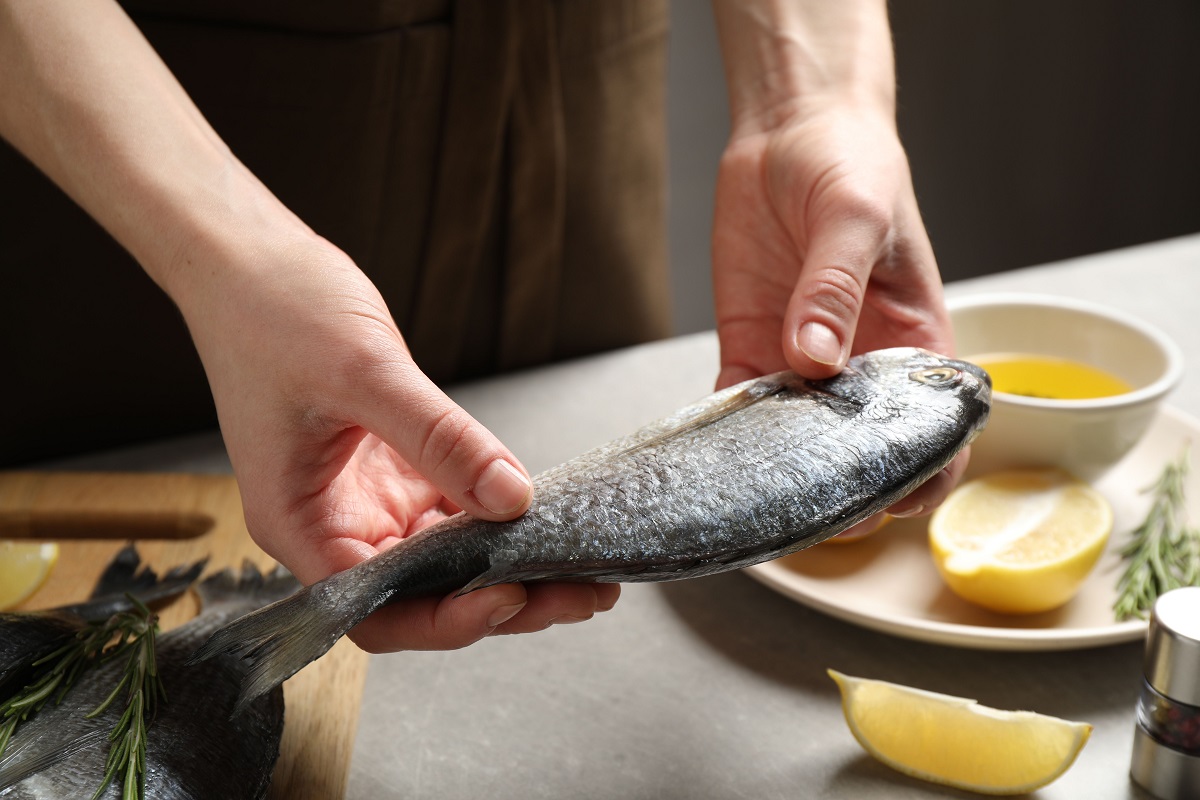 Woman,Holding,Dorada,Fish,Over,Grey,Table,,Closeup