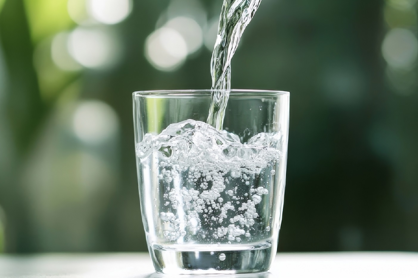 Pouring,Water,Into,A,Glass,Against,A,Green,Blurred,Background