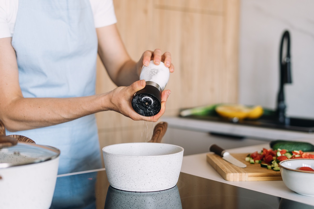 A,Woman,Adds,Black,Pepper,To,A,Pot,While,Preparing