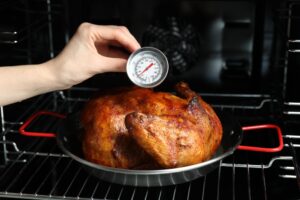 Woman,Measuring,Temperature,Of,Delicious,Baked,Turkey,In,Kitchen,,Closeup