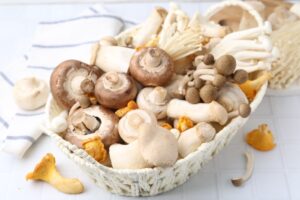 Different,Raw,Mushrooms,In,Wicker,Basket,On,White,Tiled,Table,
