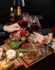 Clinking,Red,Wine,Glasses,Over,A,Gourmet,Steak,Dinner,Elegant